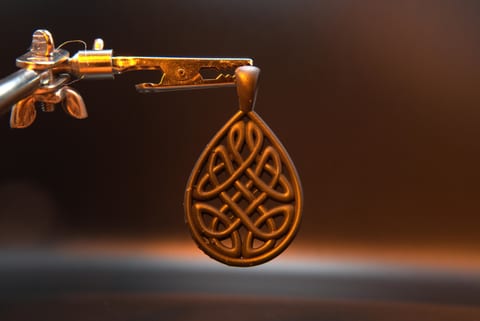 Celtic knot pendant printed in resin, hanging from a clamp with each knotwork strand separate