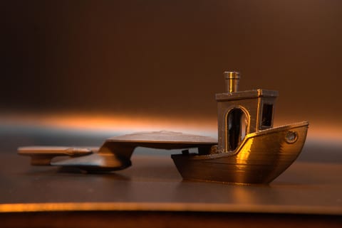 A filament-printed model boat lit from the side, its hull showing the fine horizontal banding of FDM layers