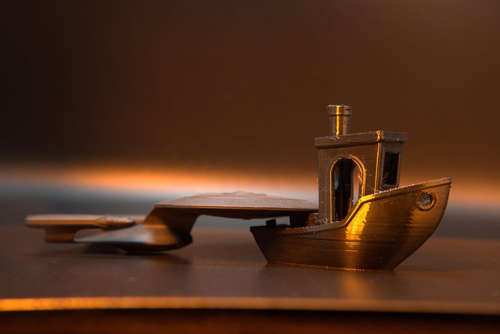 A filament-printed model boat lit from the side, its hull showing the fine horizontal banding of FDM layers
