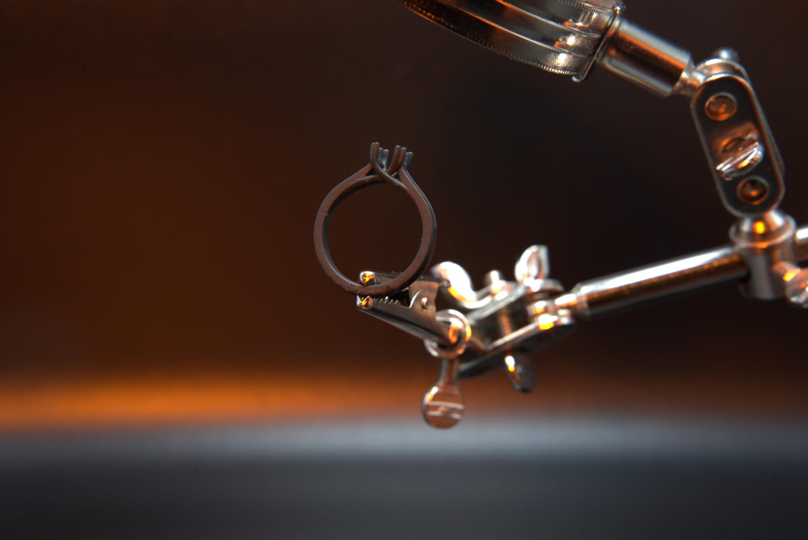 Resin 3D printed solitaire ring pattern held in a helping-hands clamp, its four-prong head thinner than the clamp jaws