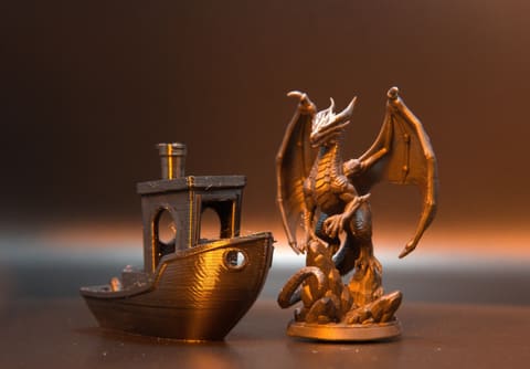 An FDM filament boat with visible layer lines beside a crisp SLA resin dragon, printed from comparable files